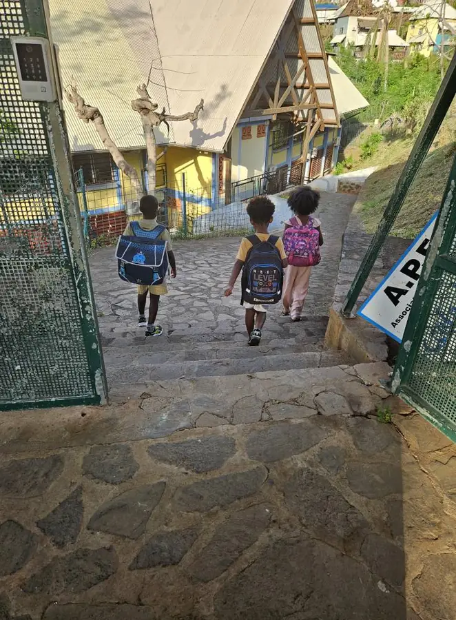 Trois élèves avec leur cartable descendent l'escalier depuis le portail de l'école